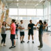 Groupe diversifié de jeunes adultes, deux femmes et deux hommes, choisissant des activités sportives dans un complexe moderne baigné de lumière naturelle.