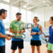 Deux hommes et deux femmes adultes comparent des raquettes de tennis dans un complexe sportif lumineux à Créteil.
